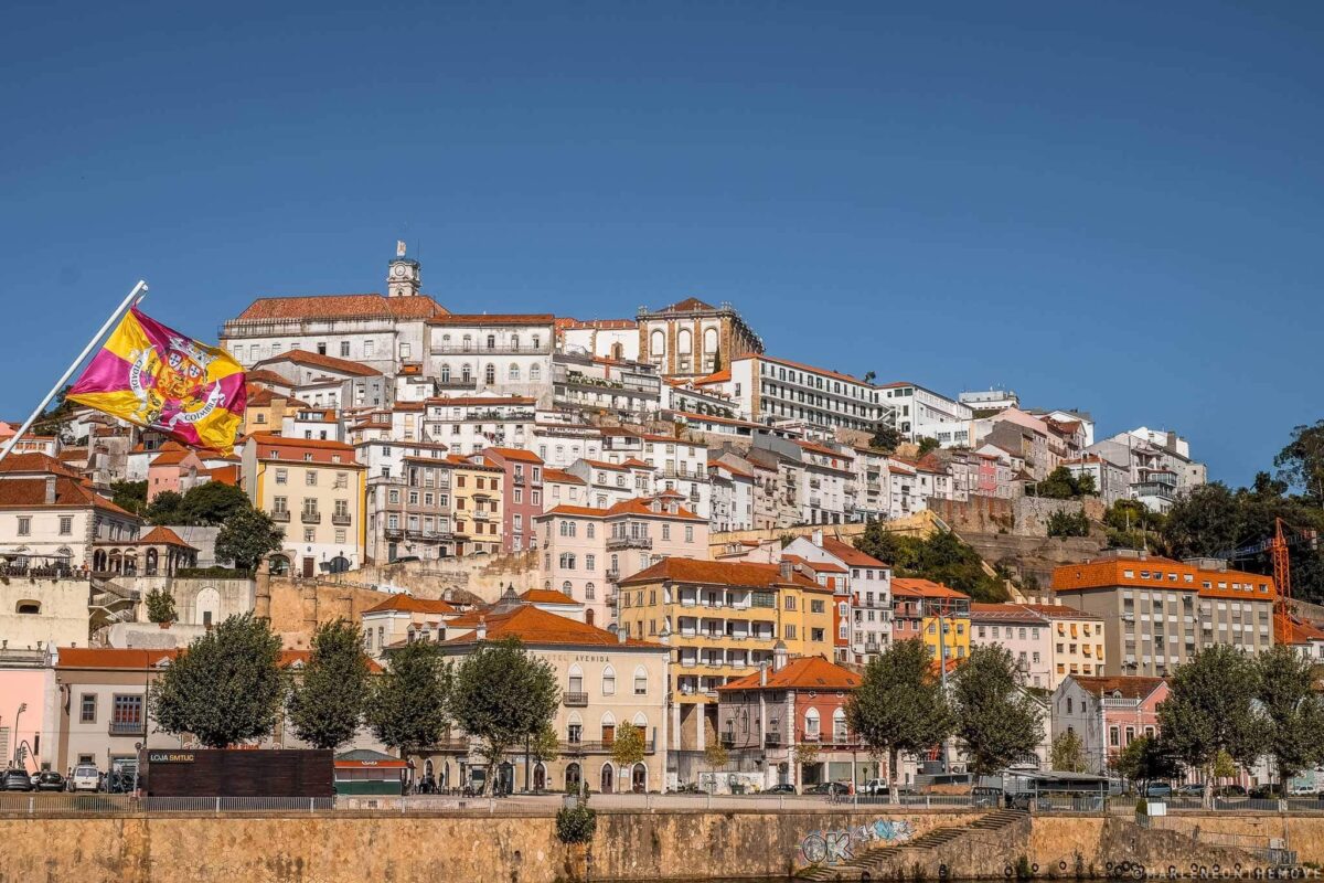 Vista della città di Coimbra dal Ponte di Santa Clara, il ponte di accesso principale alla città. Sulla sinistra si nota sventolare anche la bandiera della città di Coimbra.